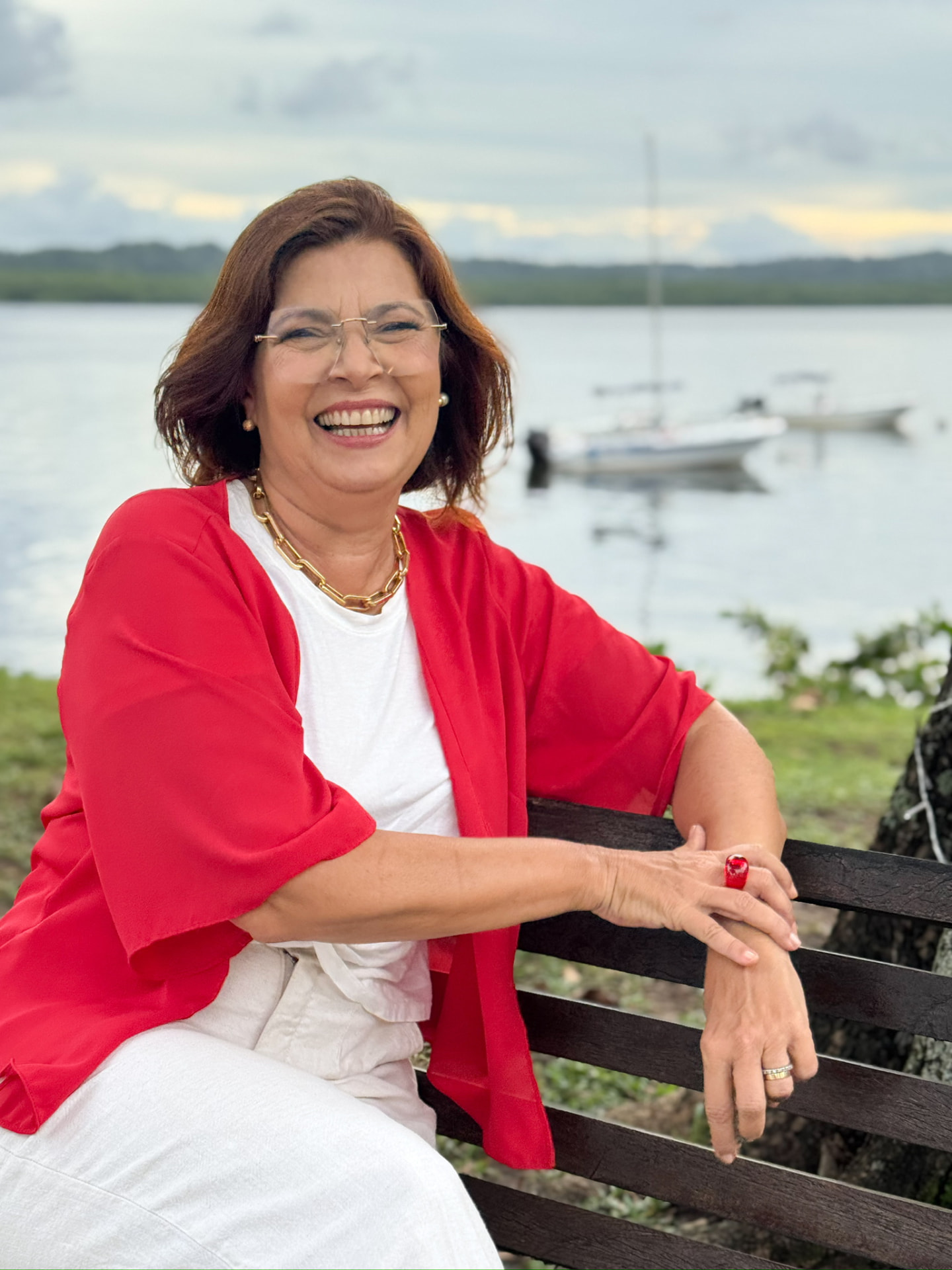 Adélia Pinheiro sorrindo sentada em um banco à beira do rio